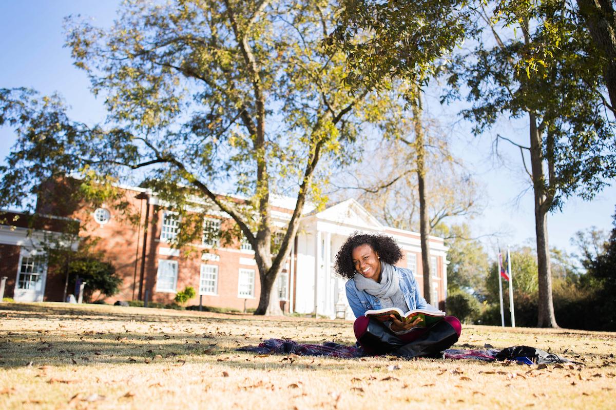 Student smiling and studying in the grass.